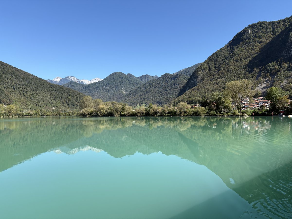 A lake with the colour of the Soca river and the Alps in the background..